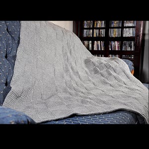 May include: A gray knitted throw blanket draped over a blue couch. The blanket has a textured weave pattern.