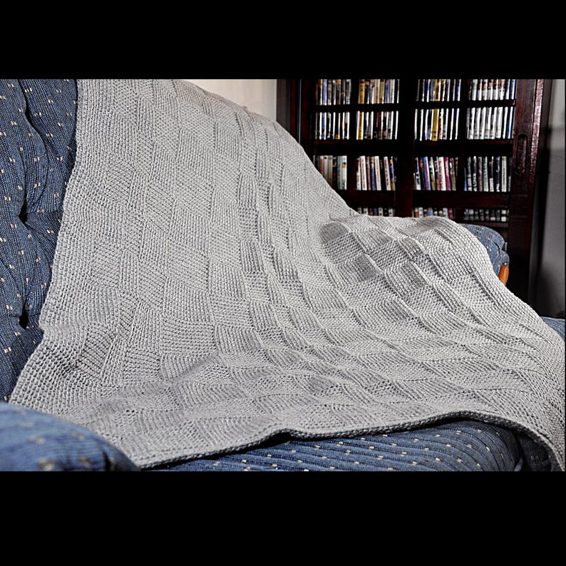 May include: A gray knitted throw blanket draped over a blue couch. The blanket has a textured weave pattern.