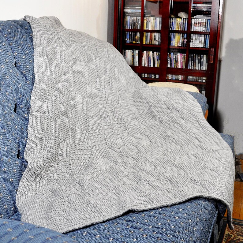 May include: A gray knitted throw blanket draped over a blue couch with a white polka dot pattern. The blanket has a woven texture and is folded over the back of the couch.