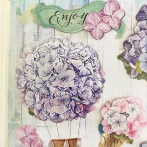 May include: Decorative stickers featuring watercolor-style hydrangea flowers in shades of purple and pink. One sticker shows a hydrangea in a hot air balloon design with a woven basket. The word "Enjoy" is written on a banner.