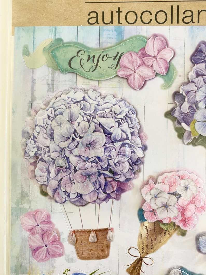 May include: Decorative stickers featuring watercolor-style hydrangea flowers in shades of purple and pink. One sticker shows a hydrangea in a hot air balloon design with a woven basket. The word "Enjoy" is written on a banner.