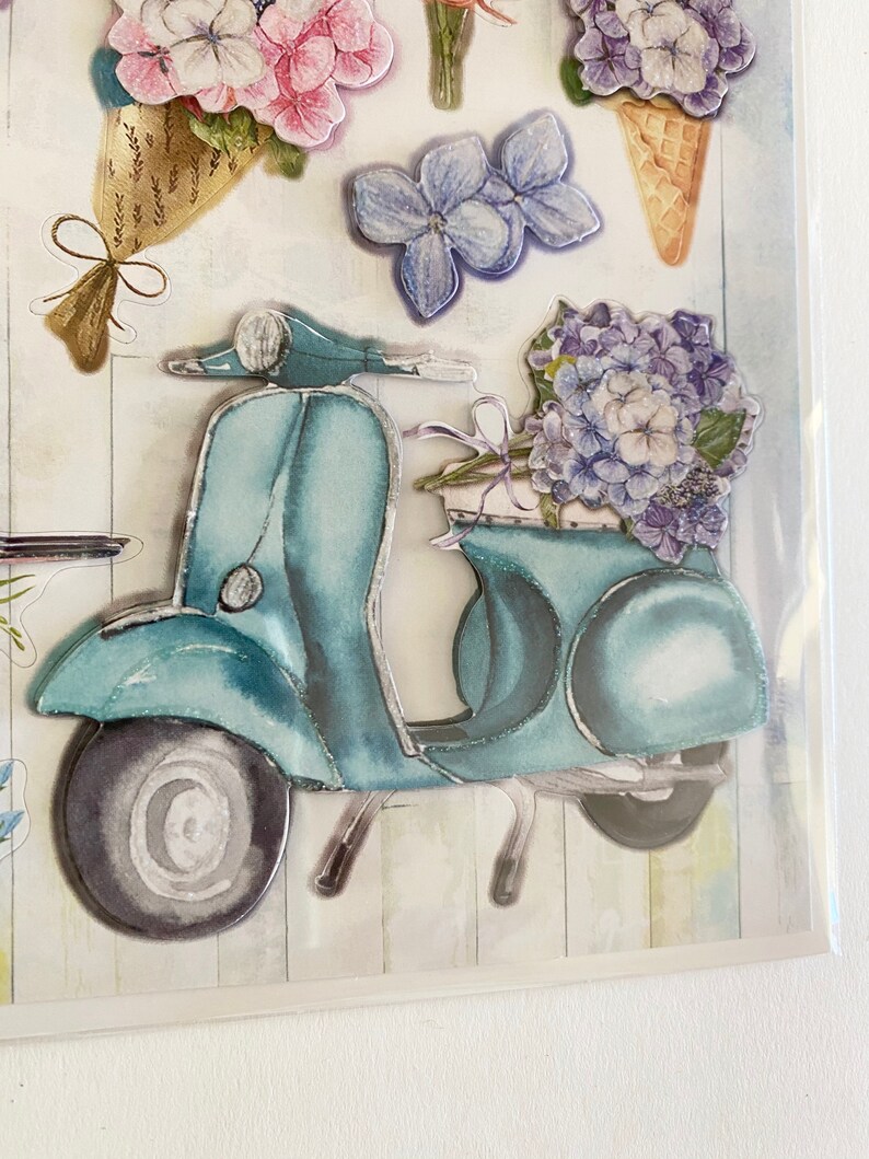 May include: Decorative stickers featuring a teal scooter carrying a bouquet of blue hydrangeas. Other stickers include pink and purple flowers, and a flower-shaped ice cream cone. The stickers have a watercolor effect.