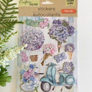 May include: A package of Crafter's Square pop-up stickers featuring floral designs, including hydrangeas, a scooter, and a teacup with a bird. The package includes the text "stickers" and "autocollants".