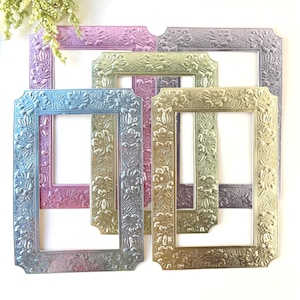 May include: A collection of ornate picture frames in various sizes and colors. The frames feature a floral design and are painted in shades of blue, pink, green, and gold. The frames are arranged on a white surface.