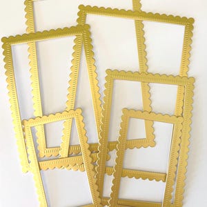 May include: A collection of gold-colored, rectangular picture frames with scalloped edges. The frames are arranged in a scattered pattern, showcasing their decorative design. The frames are empty, ready for photos or artwork.