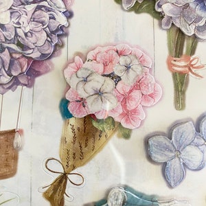May include: A collection of floral stickers featuring various hydrangea bouquets in shades of purple, pink, and white. Some bouquets are tied with ribbons, and one is in a decorative cone. A blue scooter sticker is also visible.