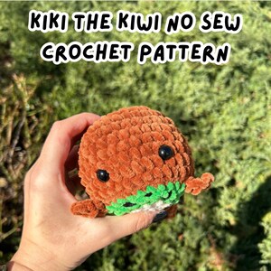 May include: A brown crocheted kiwi bird with black eyes and a green kiwi fruit design. The kiwi is being held in a hand. The text "KIKI THE KIWI NO SEW CROCHET PATTERN" is at the top of the image.