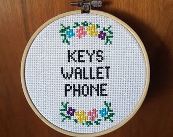 May include: A white embroidery hoop with a floral design and the text "KEYS WALLET PHONE" in black.