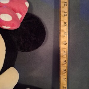 May include: A plush Minnie Mouse doll with a pink bow with white polka dots. The doll is black, white, and pink. A wooden ruler is next to the doll, measuring approximately 23 inches.