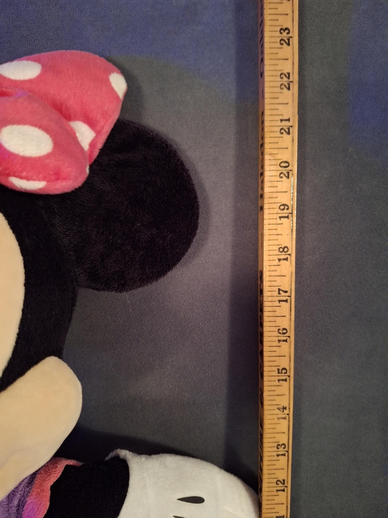 May include: A plush Minnie Mouse doll with a pink bow with white polka dots. The doll is black, white, and pink. A wooden ruler is next to the doll, measuring approximately 23 inches.