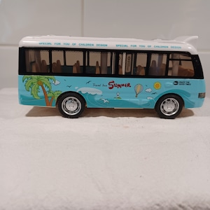 May include: A blue and white toy bus with a summer theme. The bus has a white roof and windows, and the sides are decorated with palm trees, a hot air balloon, and the words "Travel bus Summer".