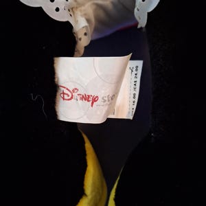 May include: A black plush toy with yellow feet and a red bow. The toy has a white collar with a scalloped edge. A Disney Store tag is visible.