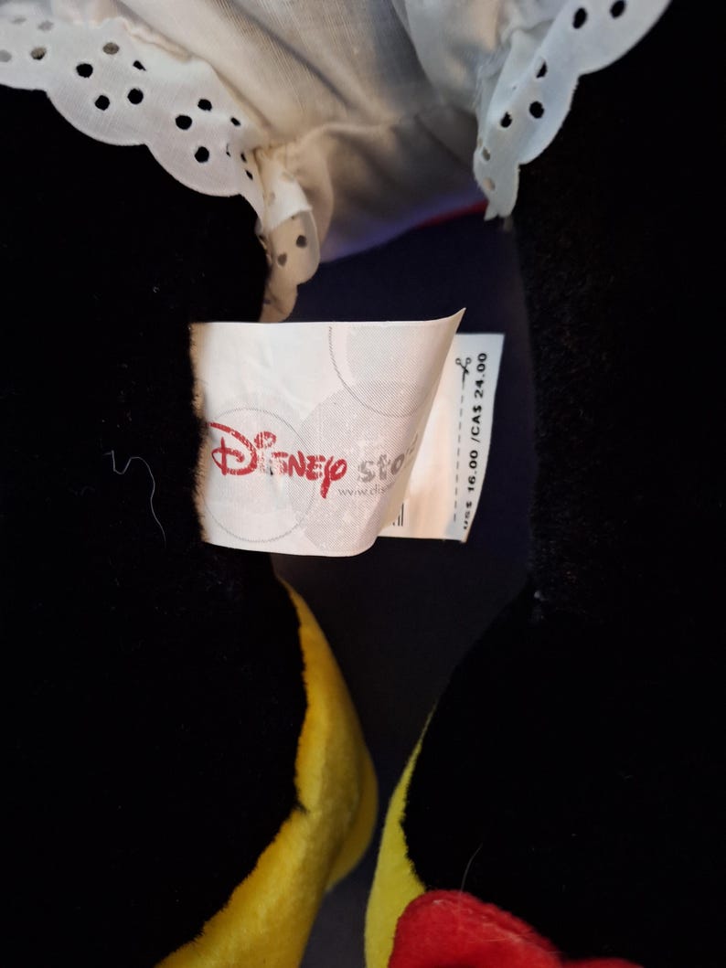 May include: A black plush toy with yellow feet and a red bow. The toy has a white collar with a scalloped edge. A Disney Store tag is visible.