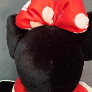 May include: A soft toy with a black head and ears, a red dress, and a red bow with white polka dots. The toy is a character from a well-known animated series.