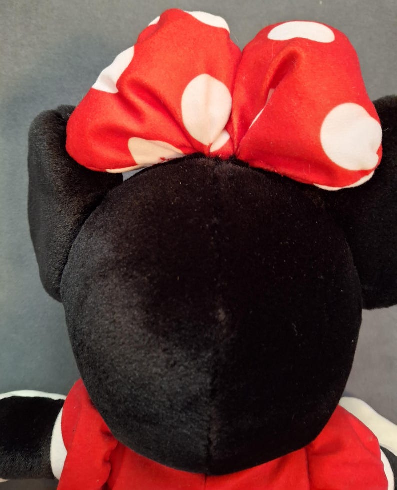 May include: A soft toy with a black head and ears, a red dress, and a red bow with white polka dots. The toy is a character from a well-known animated series.