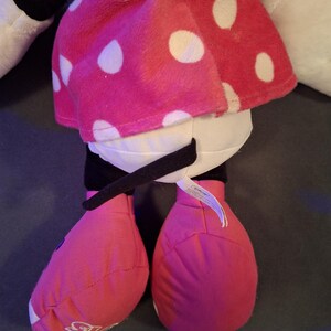 May include: A plush doll featuring a pink skirt with white polka dots, pink shoes, and black accents. The doll has white arms and a purple top. A black belt-like detail is visible. The doll is a popular character.