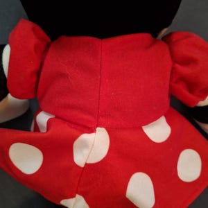 May include: A soft toy with a black head and a red dress adorned with large white polka dots. The toy has red puffed sleeves and is a character from a well-known animated series.