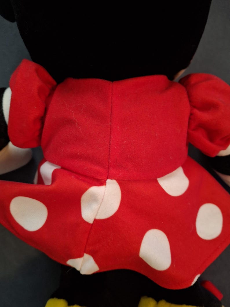 May include: A soft toy with a black head and a red dress adorned with large white polka dots. The toy has red puffed sleeves and is a character from a well-known animated series.