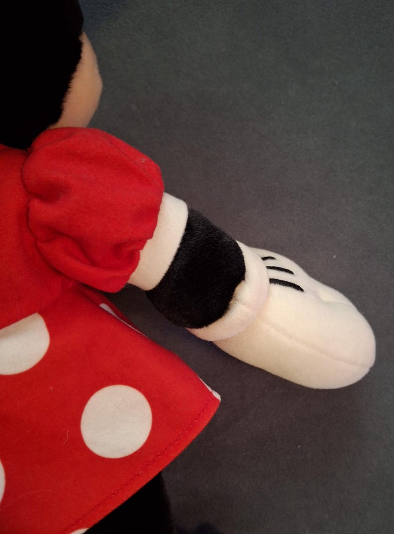 May include: A soft toy with a red dress and white polka dots, a black sleeve with a white cuff, and a white hand with black lines. The toy has a black head and is likely a cartoon character.