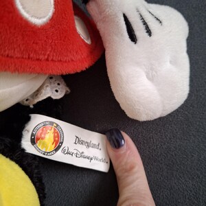 May include: Close-up of a Mickey Mouse plush toy. The toy features a red head with white accents, a white glove with black details, and a tag that reads "Disneyland Walt Disney World."