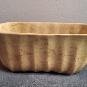 May include: A rectangular, beige ceramic baking dish with a fluted exterior. The dish has a slightly marbled appearance and a scalloped rim. The interior is smooth, and the dish appears to be unused.
