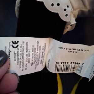 May include: A Minnie Mouse soft toy with a white lace collar. The tag reads "MADE IN CHINA/FABRIQU&Eacute; EN CHINE MINNIE 15". The toy is black with yellow accents.