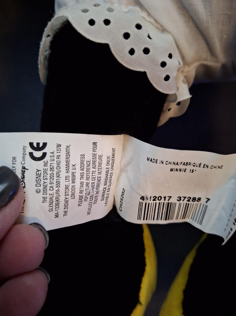 May include: A Minnie Mouse soft toy with a white lace collar. The tag reads "MADE IN CHINA/FABRIQU&Eacute; EN CHINE MINNIE 15". The toy is black with yellow accents.