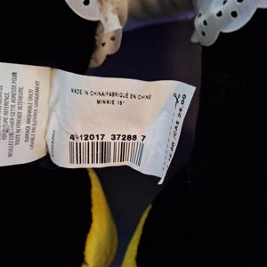 May include: A black Minnie Mouse soft toy with a white eyelet lace collar. The tag reads "MADE IN CHINA" and "MINNIE 15". The doll has yellow and red accents.