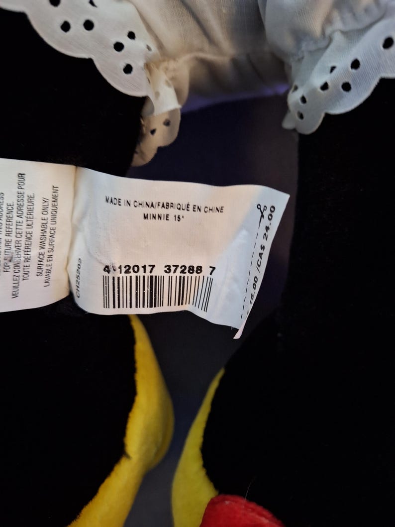 May include: A black Minnie Mouse soft toy with a white eyelet lace collar. The tag reads "MADE IN CHINA" and "MINNIE 15". The doll has yellow and red accents.