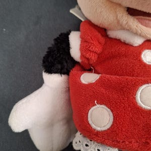 May include: A plush Minnie Mouse doll. The doll features a red dress with white polka dots, a white lace collar, and white gloves. The doll's arms and legs are black, and the face is a light tan color.