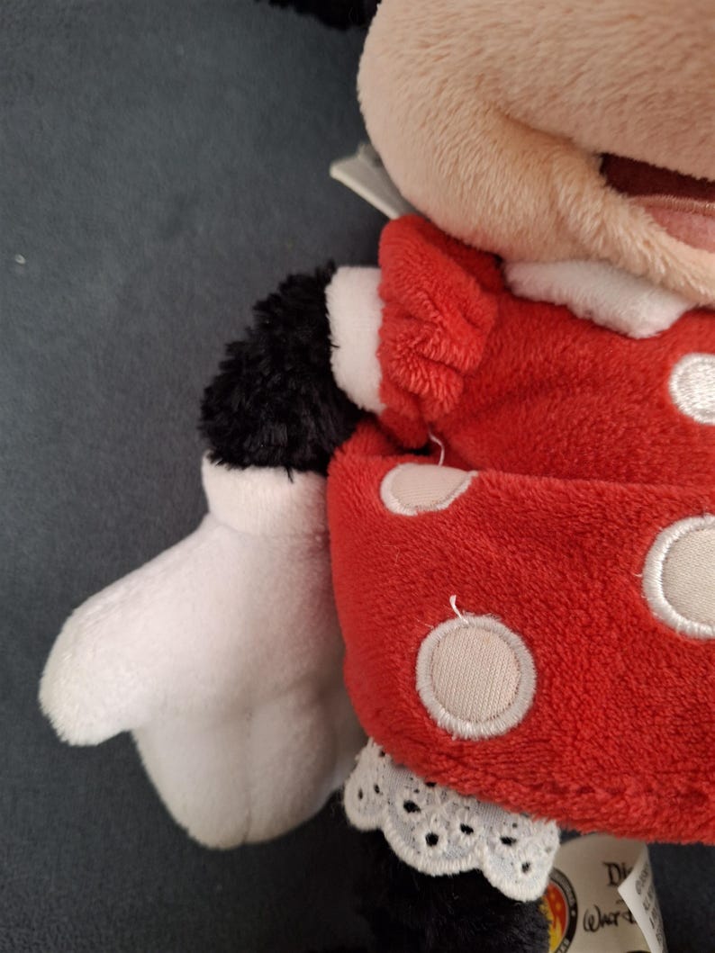 May include: A plush Minnie Mouse doll. The doll features a red dress with white polka dots, a white lace collar, and white gloves. The doll's arms and legs are black, and the face is a light tan color.