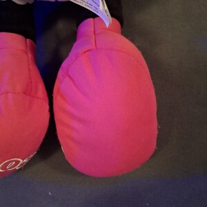 May include: Close-up of a plush toy's bright pink foot. The foot is made of soft fabric and has a rounded shape. A white tag with the Disney logo is visible. The toy is likely a character from Disney.