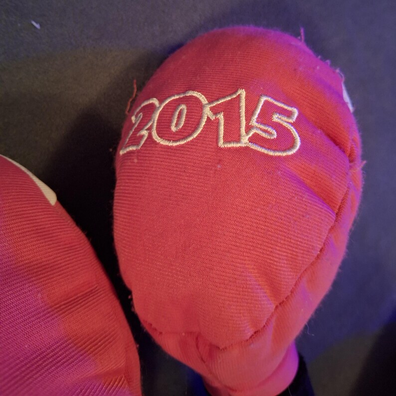 May include: Close-up of a red fabric item with the year "2015" embroidered in white. The fabric appears to be a soft material, possibly cotton or a similar textile. The item is partially visible against a dark background.