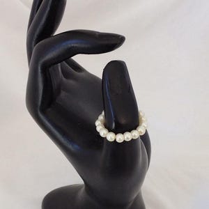 K&ouml;nnte beinhalten: Ein wei&szlig;es Perlenarmband auf einer schwarzen Handpuppe.