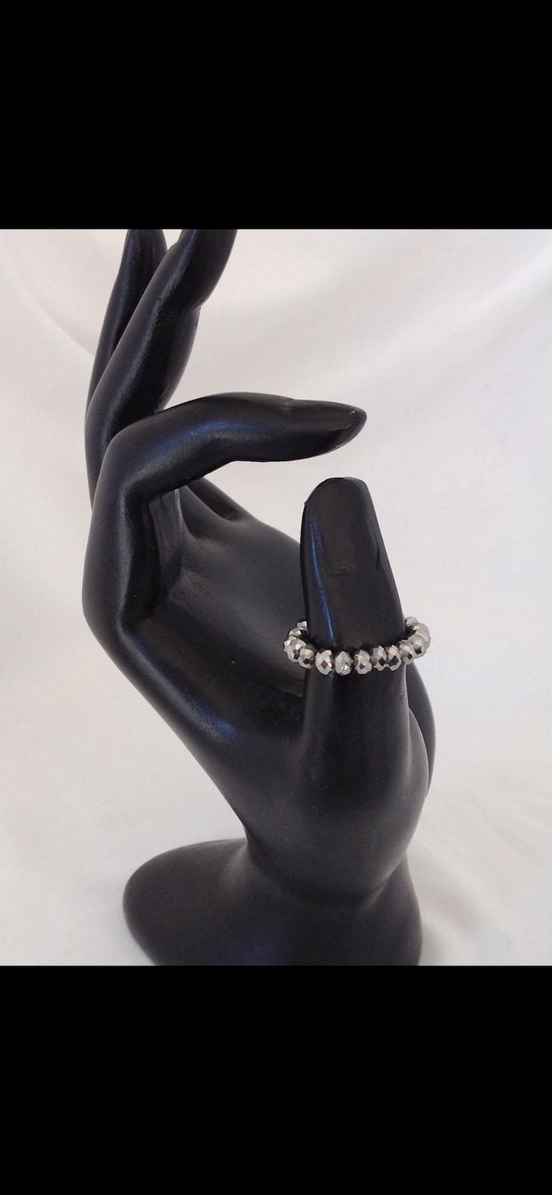 K&ouml;nnte beinhalten: Ein silberner Ring mit einem Perlenmuster. Der Ring befindet sich an einem schwarzen Handmodell.