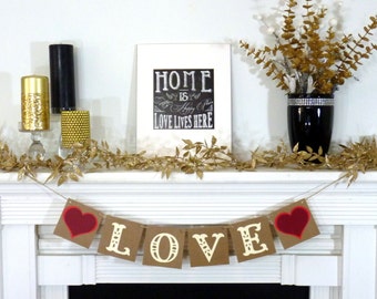 May include: A white mantelpiece decorated with a garland of gold leaves, candles, and a framed sign that reads "HOME is Happy Place LOVE LIVES HERE." A banner spelling "LOVE" with red hearts hangs below.