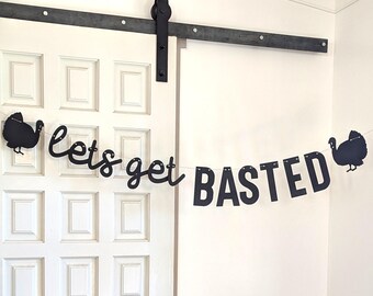 May include: A black banner with the words "lets get BASTED" strung across a white door. The banner has a turkey silhouette on each end. The door has a dark metal sliding door track and hardware.