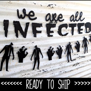 May include: Black metal banner with the words "we are all INFECTED" and zombie figures. The banner is strung across a distressed white surface, creating a spooky Halloween decoration.