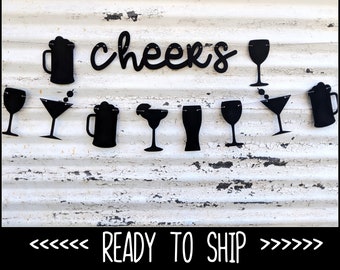 May include: Black cut-out banner with the word "cheers" and various drink silhouettes, including beer mugs, wine glasses, and martini glasses. The banner is displayed against a distressed white background. The text "READY TO SHIP" is at the bottom.
