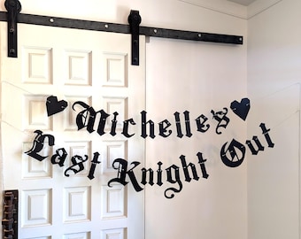 May include: Black metal banner with the text "Michelles Last Knight Out" in a gothic font, strung between two black heart shapes. The banner is hanging in front of a white door.