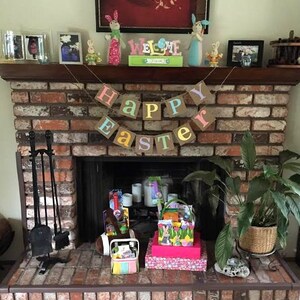 May include: A brick fireplace decorated for Easter. A banner reads "Happy Easter" above the fireplace. Easter baskets and decorations are on the hearth and mantel, including bunny figurines and a "Welcome" sign.