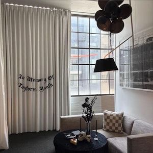 May include: A living room scene with a black round table, a gray sofa, and a large window. The curtains have the text "In Memory Of Taylors Youth". Black balloons and a black lamp hang from the ceiling. Decorative skulls and candles are on the table.