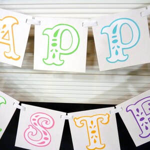 May include: A banner with the words "HAPPY EASTER" spelled out in colorful, decorative letters. The letters are orange, green, blue, pink, and purple, and are attached to a white ribbon.