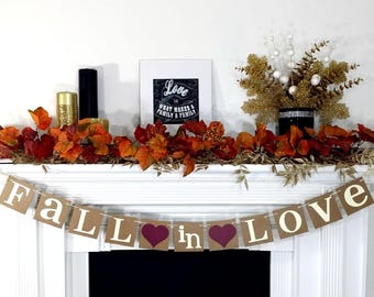 May include: A decorated mantelpiece with fall-themed decor. A banner reads "FALL in LOVE" with heart accents. The mantel is adorned with autumn leaves, candles, and a framed print that says "Love is what makes a family a family."