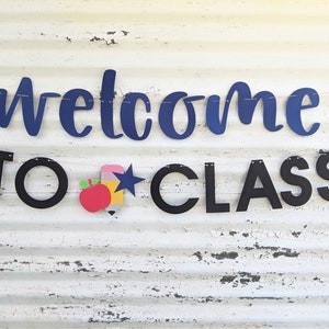 Może przedstawiać: Baner z napisem "welcome TO CLASS" w granatowych i czarnych literach. Baner zawiera czerwone jabłko, ż&oacute;łty oł&oacute;wek i niebieską gwiazdę. Baner jest nawleczony na r&oacute;żowy sznurek.