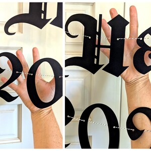 May include: Black paper banner spelling out "Happy 2023" in a gothic font. The numbers and letters are strung together with white and gray twine. The banner is held up in front of a white door.