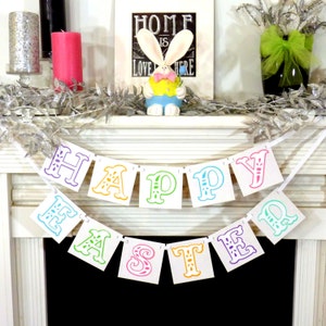 May include: A festive Easter mantel display featuring a colorful "Happy Easter" banner. The banner has multi-colored letters. A bunny figurine, candles, and decorative silver garland complete the spring-themed arrangement.
