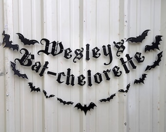 May include: Black banner with the text "Wesley's Bat-chelorette" in gothic font, adorned with bat silhouettes. The banner is strung with a thin silver chain, perfect for a Halloween or themed party.
