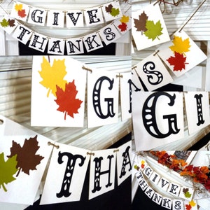 May include: A festive banner with the words "GIVE THANKS" in black, decorative lettering. The banner is strung with twine and adorned with colorful leaf cutouts in shades of red, yellow, and brown, perfect for autumn decor.