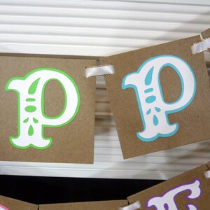 May include: A banner with brown cardstock pennants, each displaying a letter "P". The letters are white with green or blue accents. White ribbon is used to connect the pennants. The banner is likely for a party or celebration.
